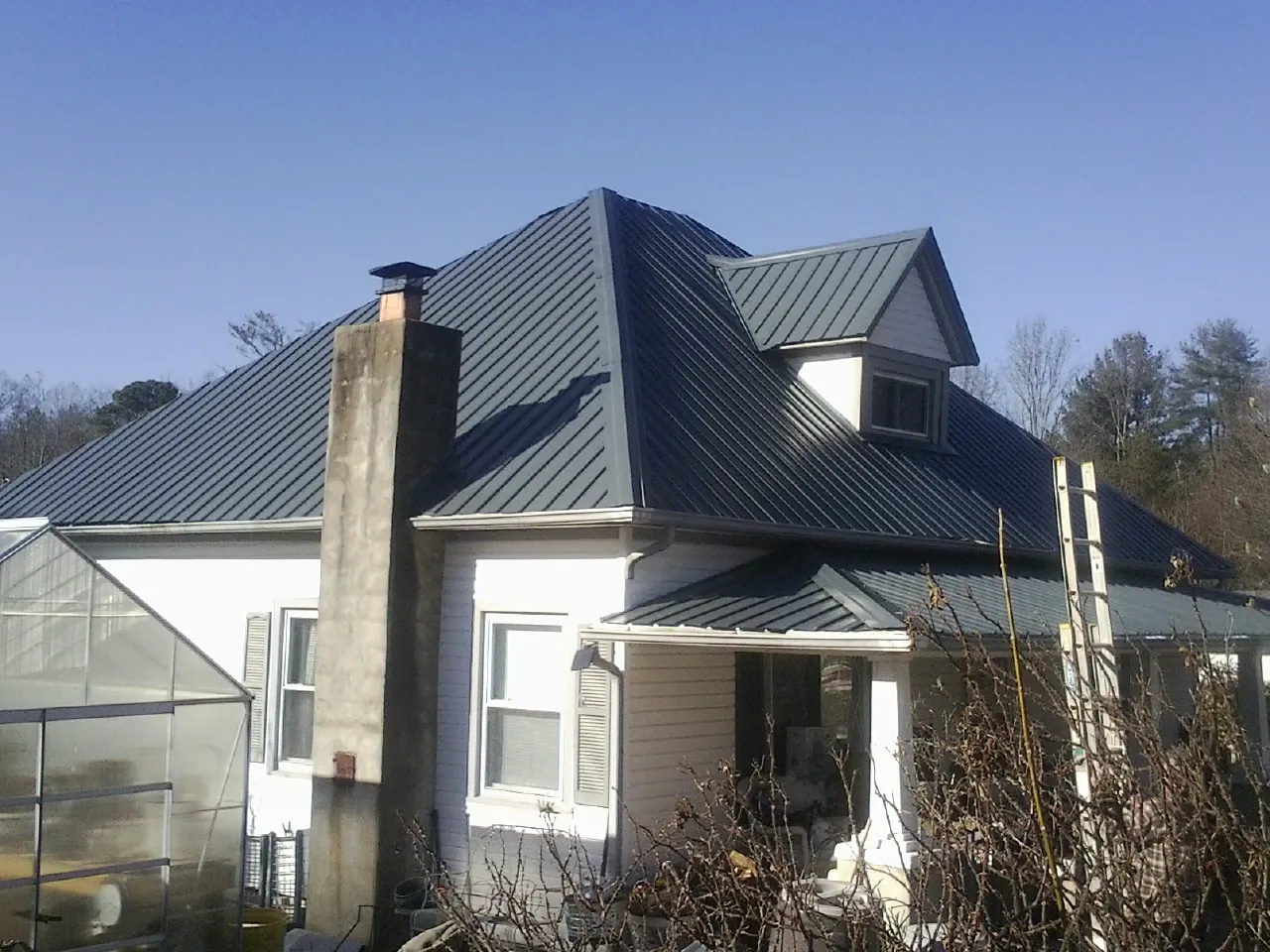 Dark blue standing seam metal roof on a white farmhouse with dormer — Slate & Tile Roof Repair by Roofing Brothers in Mentone