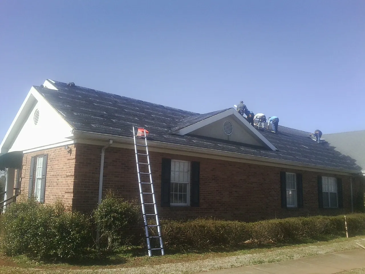 Crew tearing shingles off a brick ranch roof with a ladder set — Metal Roof Repair work by our crew in Mentone