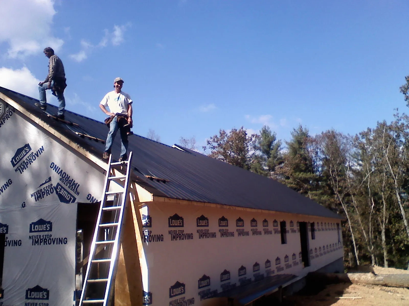 Two roofers standing on a long dark metal roof over a wrapped building in Mentone
